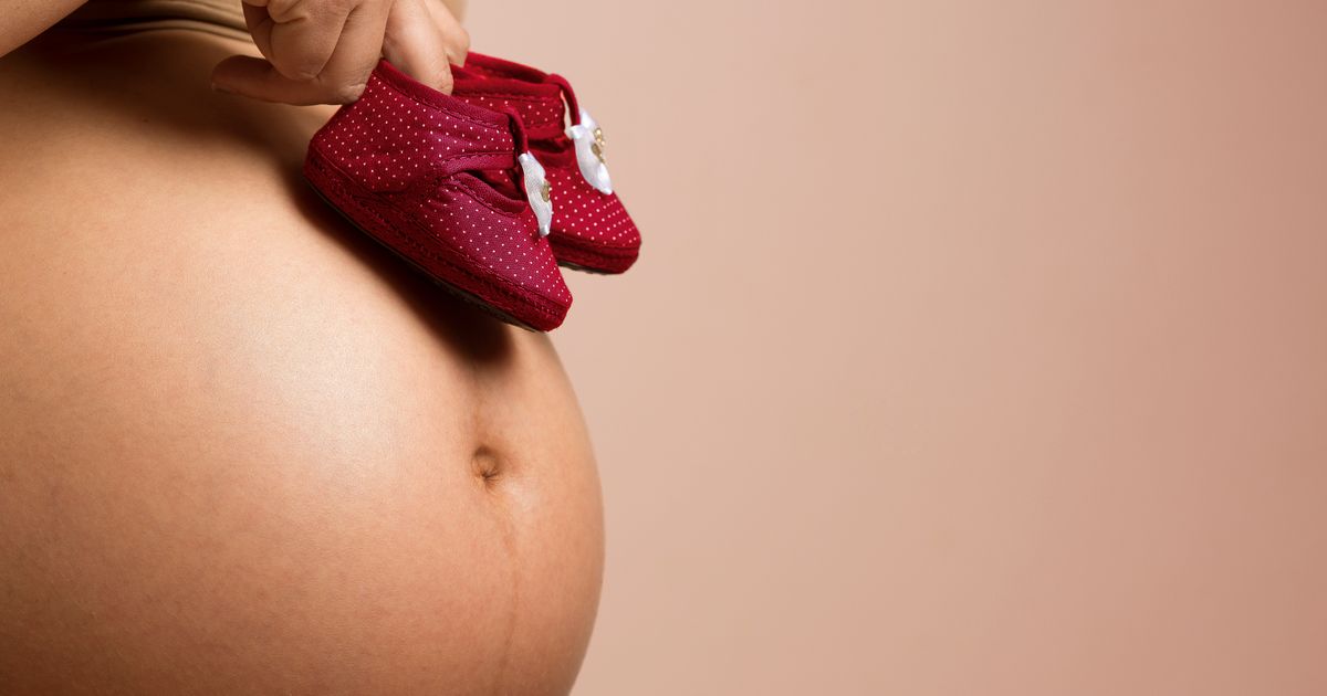 Mulher grávida segurando sapatos de bebê vermelhos sobre a barriga